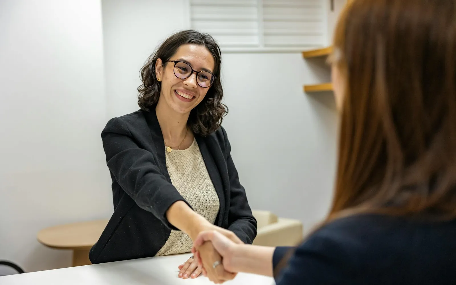 Duas mulheres apertando as mãos sobre uma mesa durante uma entrevista